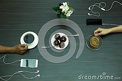 Hands holding tea and coffee cup with eclair and cellphone Stock Photo