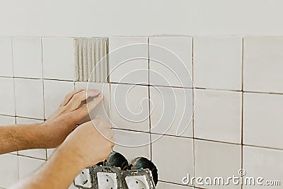 Hands laying modern square tile on adhesive close up. Worker installing stylish white tiles on plaster wall. Renovation Stock Photo