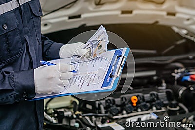 Hands of machinic man holding money, dollar banknotes and writing to the clipboard the checklist for repair machine, car service Stock Photo