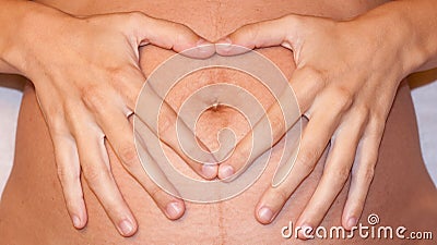 Hands making a heart-shape over a pregnant belly Stock Photo