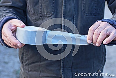hands of a man in black clothes holding a gray flyer on a roll of reinforced tape Stock Photo