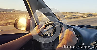 Hands of a man driver on car steering wheel. Dashboard. Windshield and side window view. Arid countryside landscape along the road Stock Photo