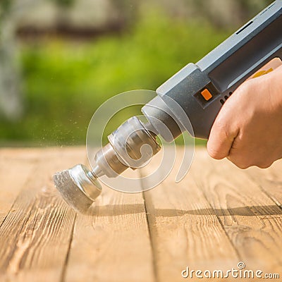 Hands man with electrical rotating brush metal disk sanding a piece of wood Stock Photo