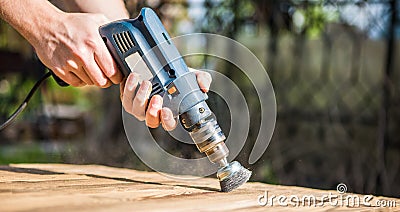 Hands man with electrical rotating brush metal disk sanding a piece of wood Stock Photo