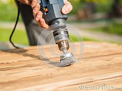 Hands man with electrical rotating brush metal disk sanding a piece of wood Stock Photo