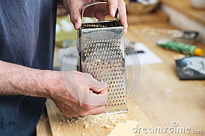 Hands of a man grating parmesan cheese on a metal grater on a wooden kitchen counter, cooking at home, copy space, selected focus Stock Photo