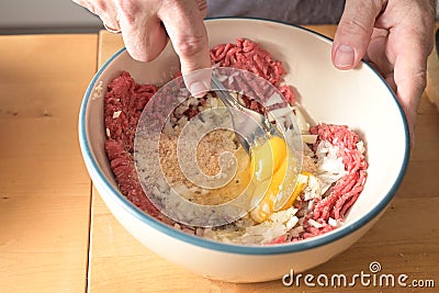 Hands of a man are mixing minced meat and other ingredients with a fork in a bowl, for making meatballs Stock Photo