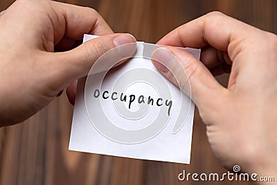 Hands of a man tearing a piece of paper with inscription occupancy Stock Photo