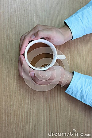 hands of the man to embrace white coffee cup on brown table and Stock Photo