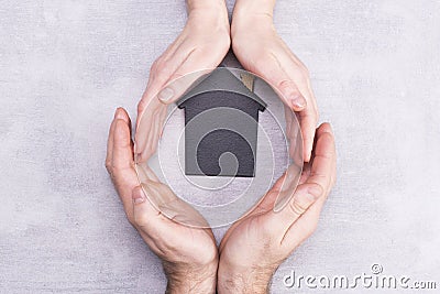 Hands of man and woman surround a model of a dark house on a gray background. Real estate and insurance concept, flat lay, top Stock Photo