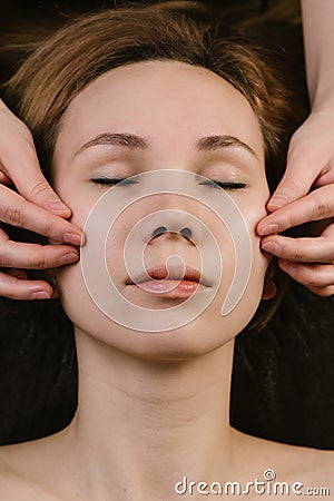 Hands massaging woman`s cheeks with fingers at asian beauty clinic. Top view Stock Photo