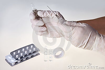 Hands of the medical worker in white gloves holding a syringe and tablets Stock Photo