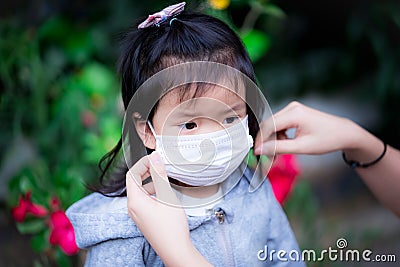 Hands of mother or guardian is wearing medical mask for Asian daughter or girl. Child looks at family. Kid aged 3 - 4 years old. Stock Photo