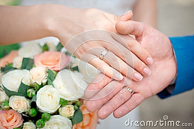 Hands of the newlyweds bride and groom with gold wedding rings close-up on a background of a wedding bouquet of roses Stock Photo