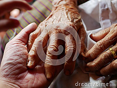 Hands of an old hard working woman on a hand of a younger man - care for elderly people Stock Photo
