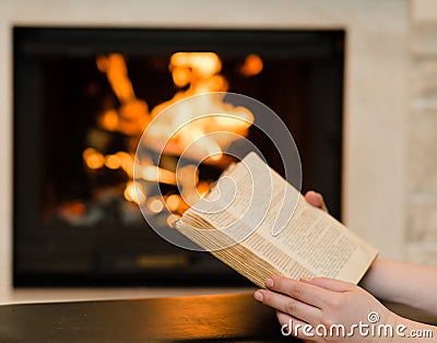 Hands with open book near the fireplace Stock Photo