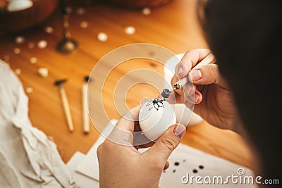 Hands painting easter egg with hot wax on background of wooden table. Modern Easter eggs with stylish wax ornaments. Happy Easter Stock Photo