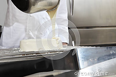 Hands pastry chef prepares a cake, cover pouring white icing, working on a stainless steel kitchen work top Stock Photo