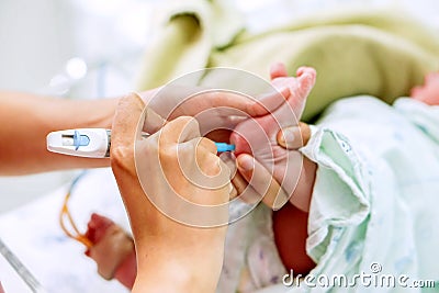 Hands of pediatric nurse holding and using Accu-Chek Fastclix needle pen for blood and glucose check stab on sick newborn baby Stock Photo