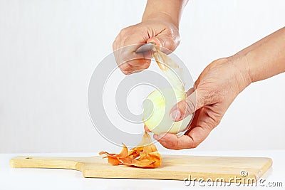 Hands peeling raw onion with a knife on a cutting board Stock Photo