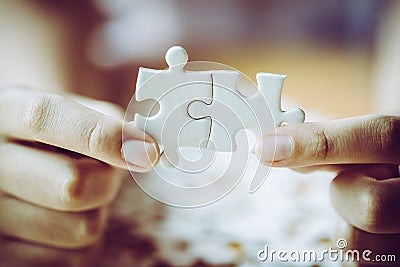 Hands of a person little child and parent playing jigsaw puzzle piece game together on wooden table at home, concept for leisure Stock Photo