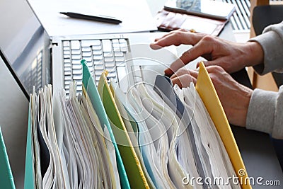 Hands of person typing on laptop computer with binders filled with papers in foreground. Selective focus Stock Photo