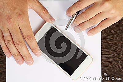 Hands, phone, white paper on the desktop, top view close-up Stock Photo