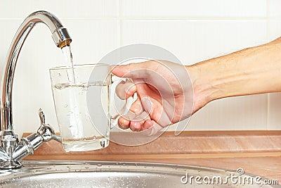 Hands pour fresh water into the glass under the tap in kitchen Stock Photo