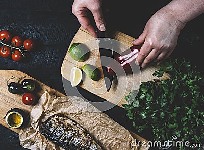 Hands in the process of cooking fish, pepper, parsley, tomato, lime on a cutting board on a black wooden background top view horiz Stock Photo