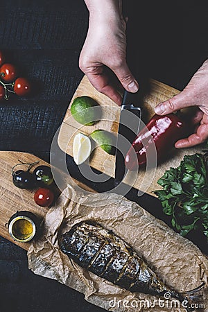 Hands in the process of cooking fish, pepper, parsley, tomato, lime on a cutting board on a black wooden background top view vert Stock Photo