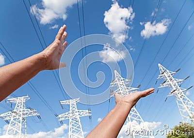 Hands reach for power transmission lines against blue sky Stock Photo