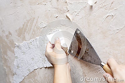 Hands remove old wallpaper from the wall with a spatula during repair in the room Stock Photo