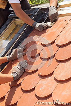 Hands of roofer laying tile on the roof. Installing natural red tile. Roof with mansard windows Stock Photo