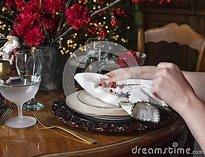 Hands setting and decorating dining table for festive winter dinner. Closeup of white napkin and red berries for Stock Photo