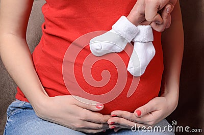 Hands in small socks on the stomach of a pregnant woman Stock Photo