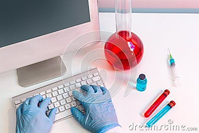 Hands with surgical gloves on a computer keyboard in a laboratory Stock Photo