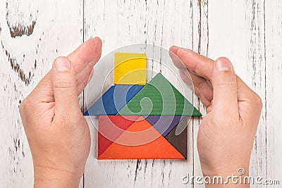 Hands surround a wooden house made by tangram home insurance concept Stock Photo