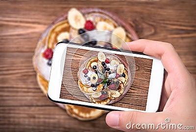 Hands taking photo pancakes with fresh fruit with smartphone. Stock Photo