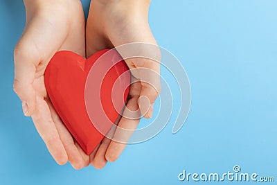 Hands of a teenager child holding a red wooden heart in their hands. Blue background Stock Photo