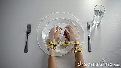 Hands tied with tapeline on empty plate, girl obsessed with counting calories Stock Photo