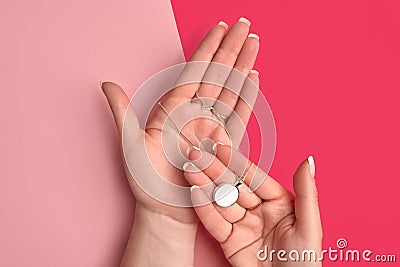 Hands of unknown young lady are holding shiny silver or platinum blank pendant on a chain against colorful studio Stock Photo