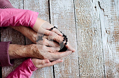 Hands of unrecognizable grandmother and her granddaughter holding rosary Stock Photo