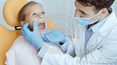 Hands of unrecognizable pediatric dentist making examination procedure for smiling cute little girl Stock Photo