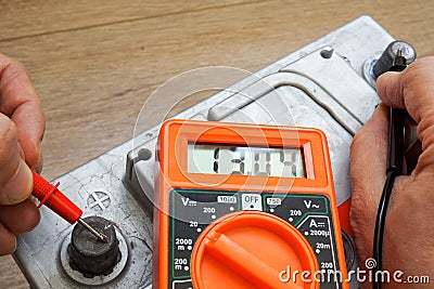 Hands with voltmeter check the charge level of the car battery. Stock Photo