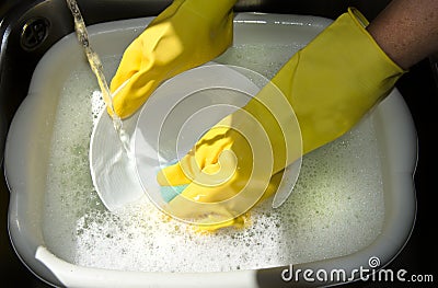Hands washing up dishes in yellow gloves Stock Photo