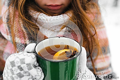 Hands in white mittens, holds a green mug of tea, and snow in winter Stock Photo