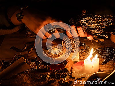 In the hands of the witches bunch of dry herbs for divination. The light from the candles on the old magic table. Attributes of Stock Photo