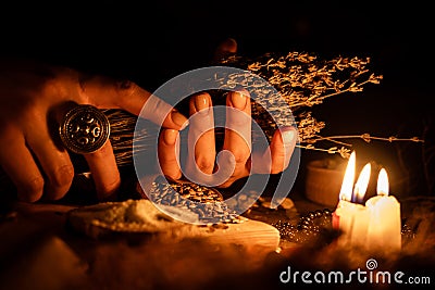 In the hands of the witches bunch of dry herbs for divination. The light from the candles on the old magic table. Attributes of Stock Photo