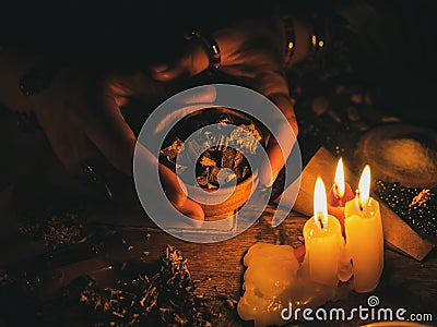 In the hands of the witches roots from plants for divination. The light from the candles on the old magic table. Attributes of Stock Photo