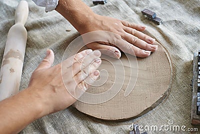 hands of a woman artisan ceramist kneading a layer of clay on the table close-up Stock Photo